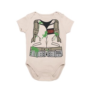 May include: A beige baby onesie with a green and brown illustration of a ghostbuster's uniform. The text "VENKMAN" is printed on the chest.