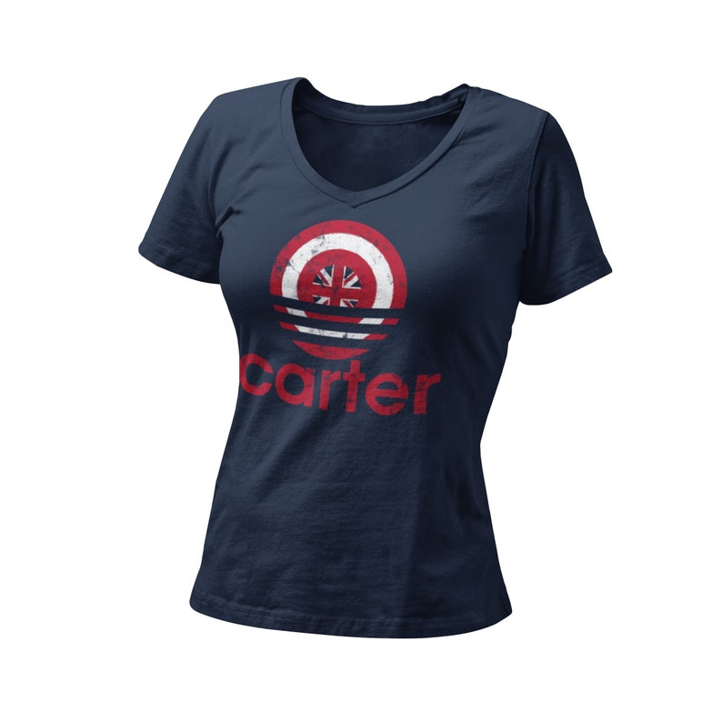 Op de afbeelding: Een marineblauw t-shirt met V-hals en een rood, wit en blauw cirkelontwerp met een Union Jack-vlag. Het woord "carter" is in rood onder de cirkel gedrukt.