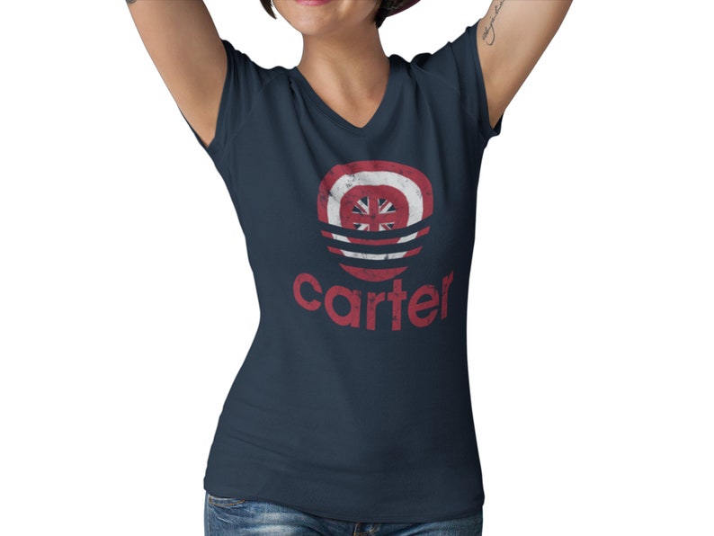 Op de afbeelding: Een marineblauw v-hals T-shirt met een rode, witte en blauwe distressed graphic van een cirkel met een ster en het woord "carter" eronder.