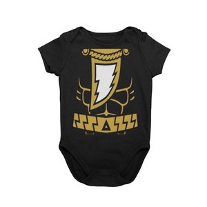May include: Black baby onesie with a gold lightning bolt and muscle design. The onesie has a gold belt with a triangle in the center.
