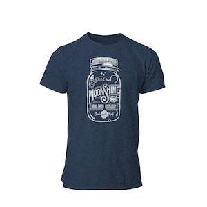 May include: A navy blue t-shirt featuring a white graphic of a mason jar with the text "Muskrat Moonshine Briar Patch Distillery" and a small muskrat graphic.