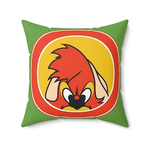 Puede incluir: Almohada verde con un círculo rojo y amarillo que presenta un pájaro rojo de dibujos animados con un pico amarillo y ojos enojados.