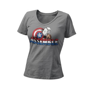 Puede incluir: Camiseta gris de cuello en V con un gr&aacute;fico del escudo del Capit&aacute;n Am&eacute;rica y el martillo de Thor con el texto "ASSEMBLE" debajo.
