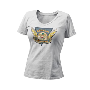 以下が含まれることがあります： カラフルなグラフィックが特徴の白いVネックTシャツ。「Cranium Command」の文字と、軍服を着た漫画のキャラクターが描かれています。デザインは三角形と翼のモチーフの中に配置されています。