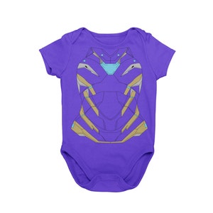 May include: A purple baby bodysuit with a graphic design resembling a superhero's armor. The design features gold, light blue, and gray accents. The bodysuit is made of soft material and has short sleeves.