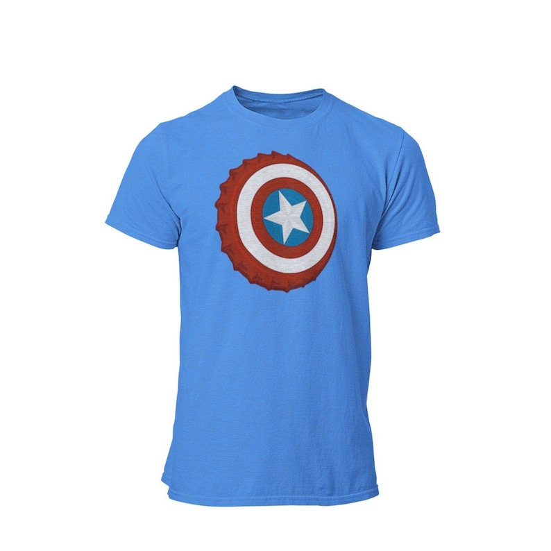 May include: A light blue t-shirt featuring a graphic of a bottle cap with a red, white, and blue shield design and a white star in the center. The shirt has short sleeves and a crew neck.