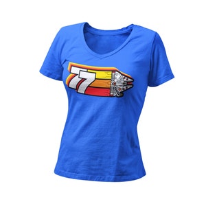 Pode incluir: Uma camiseta azul com um gráfico retrô do número 77 e uma nave espacial. O gráfico é em amarelo, laranja e vermelho.