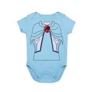 Puede incluir: Un body de bebé azul claro con una imagen de dibujos animados de un personaje que lleva una capa y una joya roja con un símbolo de gato negro.