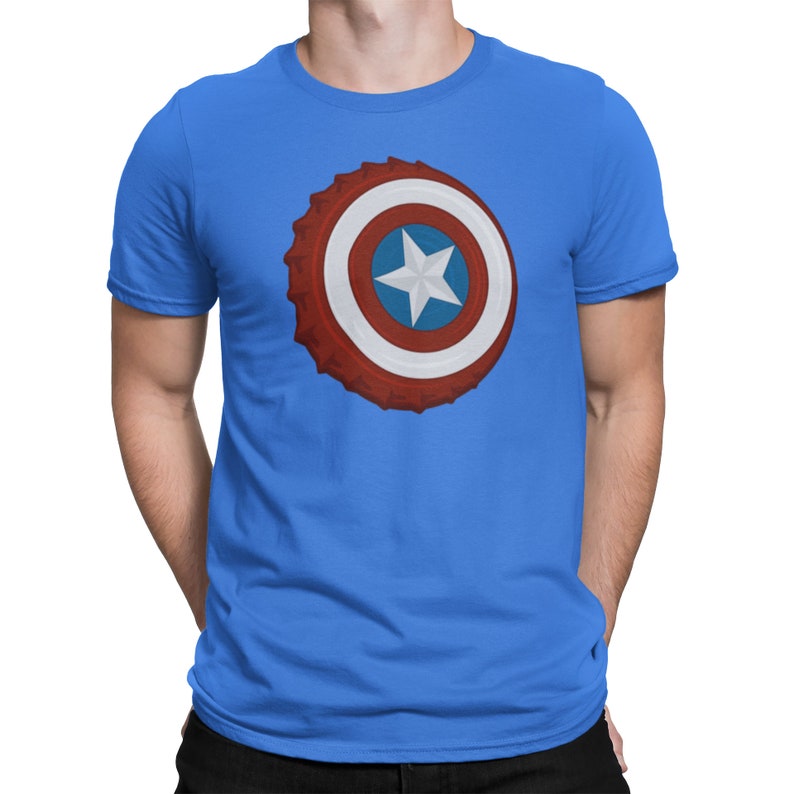 May include: Blue crew neck t-shirt featuring a graphic of a shield with red, white, and blue concentric circles and a white star in the center. The shield design is reminiscent of a bottle cap.