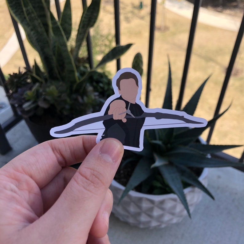 May include: A sticker featuring a stylized illustration of a person holding a bow and arrow. The character is depicted in a black outfit, with a bow drawn back, ready to shoot. The sticker has a white border.
