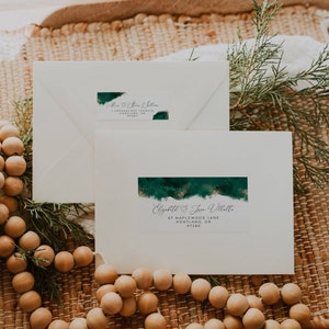 Pode incluir: Dois envelopes brancos com desenhos de aquarela verde e detalhes de glitter dourado. O envelope superior tem o texto "Ann & Steve Williams" e o envelope inferior tem o texto "Elizabeth & Jean Villatte 67 Maplewood Lane Portland, OR 97280".