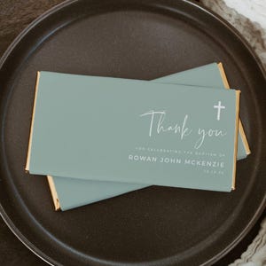 May include: A light blue thank you card with a white cross and the text "Thank you for celebrating the baptism of Rowan John McKenzie 10.10.25"