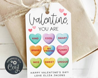 Op de afbeelding: Een witte Valentijnsdag cadeaulabel met een bruine touwstrik. Het label leest "Valentine, YOU ARE" boven kleurrijke snoepharten met woorden als "KIND" en "COOL". Het label zegt ook "HAPPY VALENTINE'S DAY! LOVE ELIZA JACOBS".