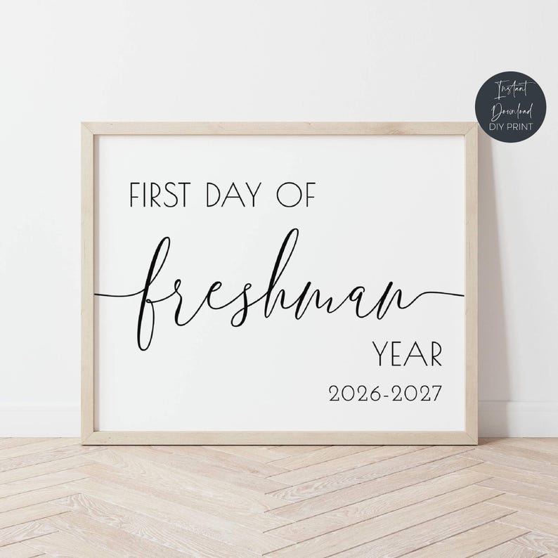Op de afbeelding: Een ingelijste witte print met zwarte tekst: "FIRST DAY OF freshman YEAR 2026-2027". De print zit in een licht houten frame. Een kleine, donkerblauwe cirkel rechtsboven heeft de woorden "Instant Download DIY Print".