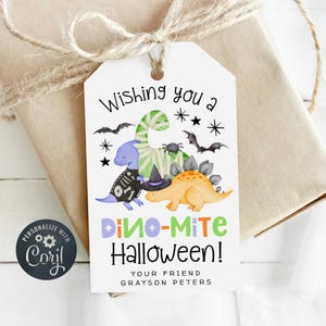 May include: A white gift tag with a Halloween dinosaur theme. The tag features a green, blue, and orange dinosaur illustration with the text "Wishing you a Dino-Mite Halloween!" and the name "Grayson Peters".