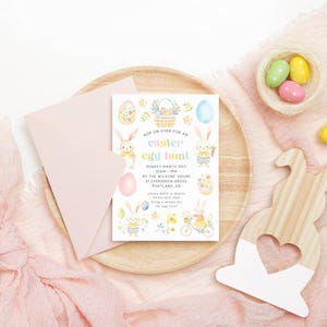 May include: An Easter-themed invitation with the text "Hop on over for an Easter egg hunt" and illustrations of bunnies and eggs. The invitation is on a wooden tray with a pink envelope and decorative wooden bunny.