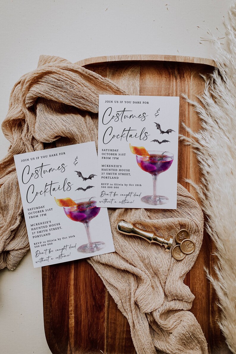 K&ouml;nnte beinhalten: Zwei wei&szlig;e Einladungskarten mit schwarzem Text und einer Aquarell-Illustration eines Cocktailglases mit einem violetten Getr&auml;nk und einer Orangenscheibe. Der Text auf den Karten lautet "Join us if you dare for Costumes & Cocktails" und enth&auml;lt Datum, Uhrzeit, Ort und RSVP-Informationen. Die Karten liegen auf einer Holzoberfl&auml;che mit einem goldenen Siegel und einem goldenen Stoff.