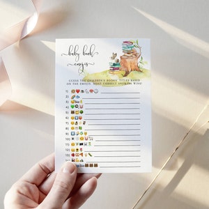 Puede incluir: Una tarjeta de juego de baby shower imprimible con el t&iacute;tulo "Baby Book Emojis". El juego pide a los invitados que adivinen los t&iacute;tulos de los libros infantiles en funci&oacute;n de los emojis. La tarjeta presenta una ilustraci&oacute;n de acuarela de una pila de libros sobre un toc&oacute;n de &aacute;rbol con un conejo.