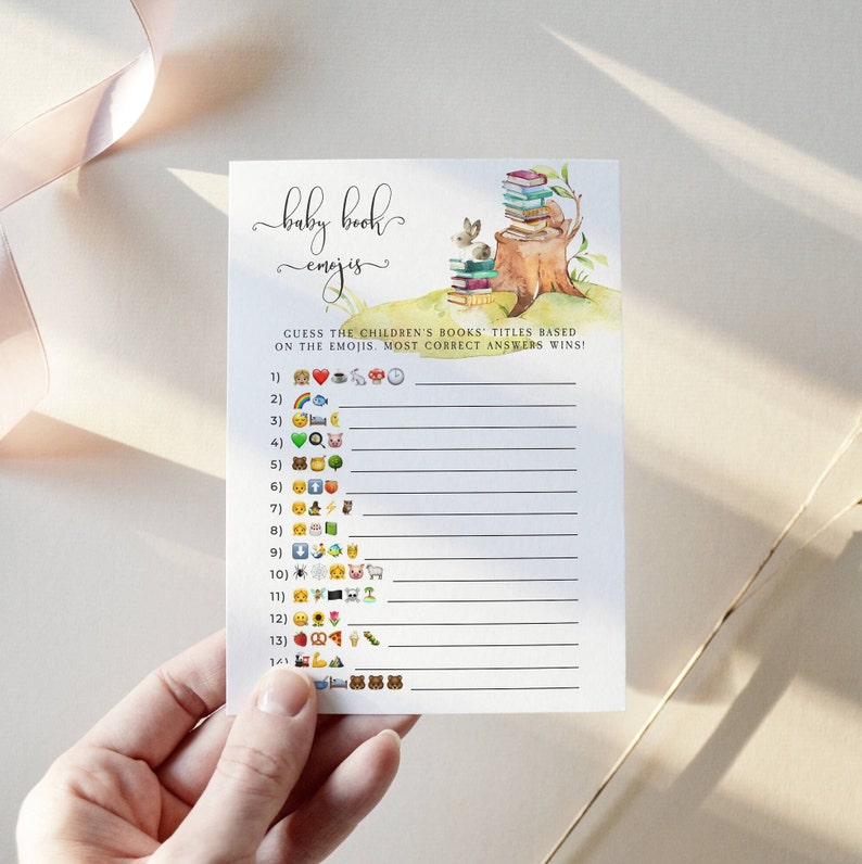 Puede incluir: Una tarjeta de juego de baby shower imprimible con el t&iacute;tulo "Baby Book Emojis". El juego pide a los invitados que adivinen los t&iacute;tulos de los libros infantiles en funci&oacute;n de los emojis. La tarjeta presenta una ilustraci&oacute;n de acuarela de una pila de libros sobre un toc&oacute;n de &aacute;rbol con un conejo.