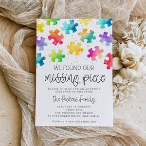 May include: A rectangular white invitation card featuring a colourful watercolour puzzle piece pattern at the top with gold speckles. The text reads: WE FOUND OUR missing piece, PLEASE JOIN US FOR AN ADOPTION CELEBRATION HONOURING the Pickens Family, SATURDAY 12 FEBRUARY FROM 2PM, THE PICKENS RESIDENCE, 76 EVERGREEN DRIVE, SNOHOMISH, RSVP to Alisa (555) 000 000.