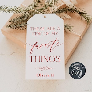 Może przedstawiać: Biała etykieta prezentowa z czerwonym tekstem "THESE ARE A FEW OF MY favorite THINGS with love Olivia H". Etykieta jest przymocowana do zapakowanego prezentu, ozdobionego zielenią.