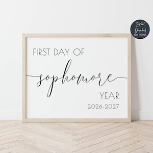 May include: A framed print with the text "FIRST DAY OF sophomore YEAR 2026-2027" in black font on a white background. The frame is a light wood color. A small circular logo in the upper right corner reads "Instant Download DIY Print."