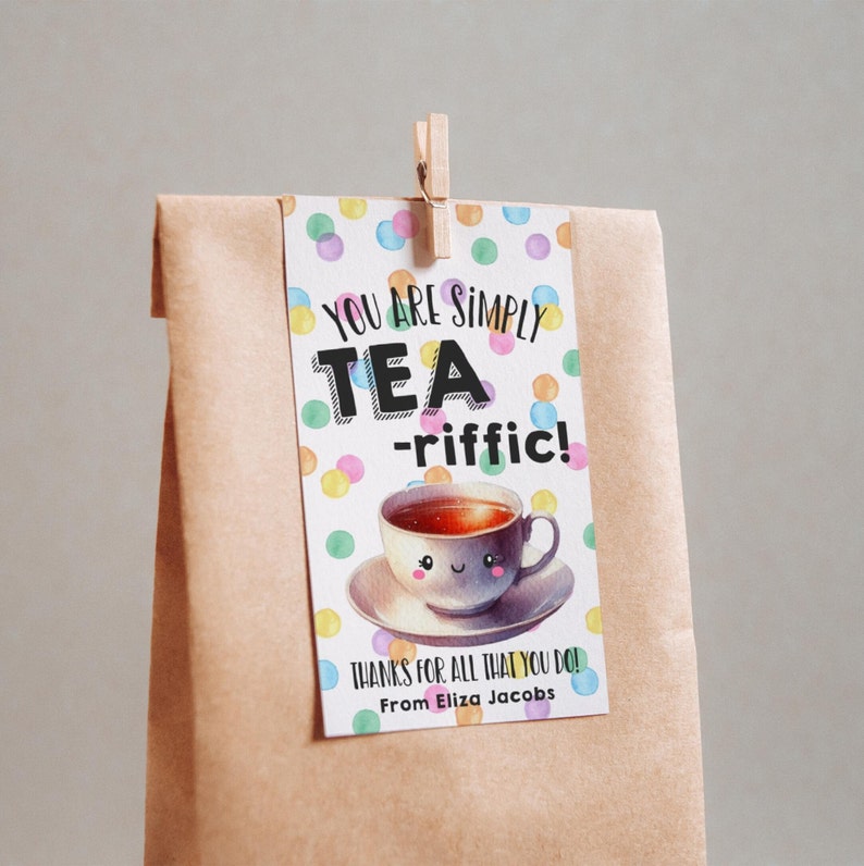 May include: A brown paper bag with a colorful gift tag attached. The tag features a cartoon teacup with a smiling face and the text "You are simply tea-riffic! Thanks for all that you do! From Eliza Jacobs."