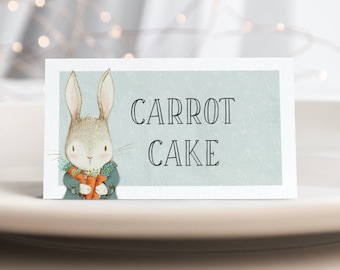 Puede incluir: Una etiqueta de comida imprimible azul claro y blanca con un conejito de dibujos animados sosteniendo una zanahoria. El texto en la etiqueta dice "CARROT CAKE".