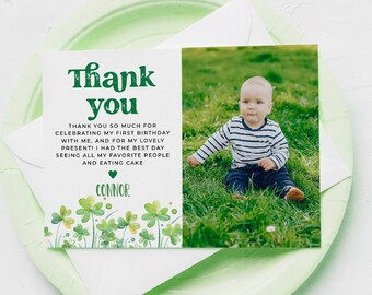 May include: A thank you card with a photo of a baby in a striped shirt sitting in grass. The card has green text that reads "Thank you" and a message about celebrating a first birthday. The card is on a green plate.