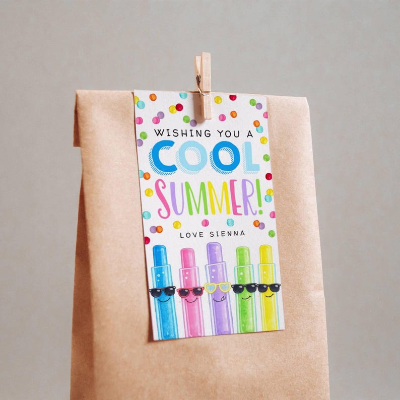 May include: A brown paper gift bag with a tag that says "Wishing You a Cool Summer!" in colorful text. The tag features cartoon crayons wearing sunglasses. The tag is held by a wooden clip.