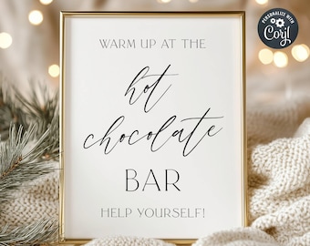 May include: A white sign with a gold frame that says "Warm up at the hot chocolate bar. Help yourself!" The sign is sitting on a white fuzzy blanket.