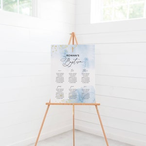 May include: A baptism seating chart on a wooden easel. The sign has a watercolor background in shades of blue and gold. The text "Rowan's Baptism" is displayed at the top, with guest names organized in columns below. A gold cross is at the top.
