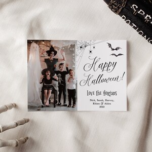 May include: A rectangular Halloween greeting card featuring a photograph of a family in costumes on the left and text on the right. The text reads Happy Halloween! Love the Morgans, Nick, Sarah, Harvey, Rhian & Aiden 2022, with spiderweb and bat illustrations.