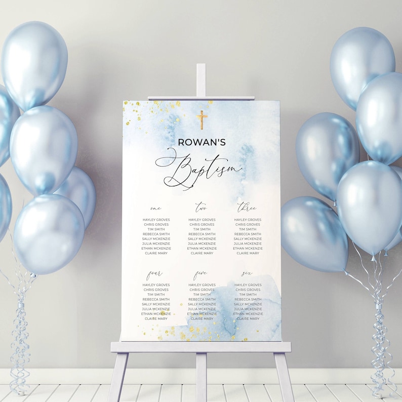May include: A baptism seating chart on an easel, featuring a watercolor design with blue and gold accents. The chart displays names organized by table numbers, with a cross at the top. Light blue balloons frame the sign.