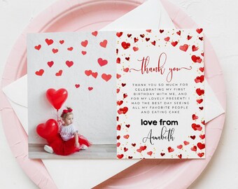 May include: A folded greeting card with a photo of a child holding heart-shaped balloons, surrounded by red hearts. The card reads "thank you" and includes a message and the name "Annabeth". The card is on a pink plate.