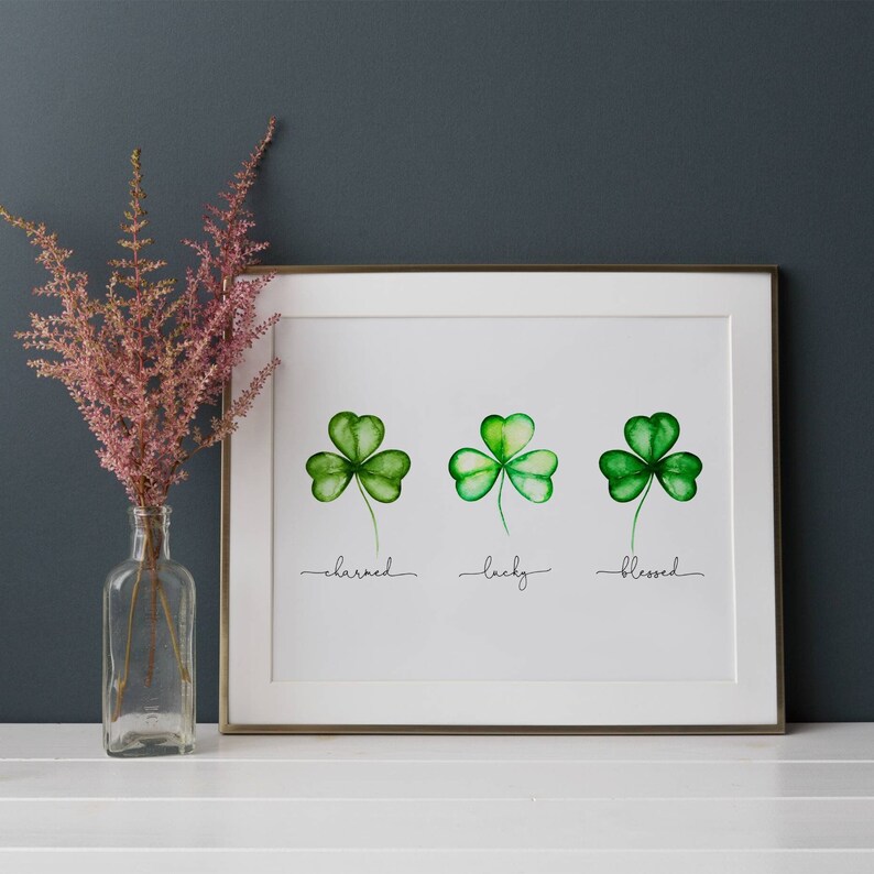 May include: A framed print with three green shamrocks, each with a different word underneath: "charmed", "lucky", and "blessed".