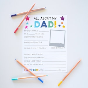 May include: A white paper questionnaire titled ALL ABOUT MY DAD! with colorful stars, blank lines for writing, and a square frame labeled HERE IS MY DAD. The sheet is surrounded by several colored pencils in shades of blue, pink, and yellow.