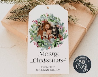 Peut inclure: Une étiquette cadeau de Noël blanche avec une couronne verte et des baies rouges. Une photo de deux enfants se trouve au centre de la couronne. Le texte "Joyeux Noël" est sous la couronne. Le texte "De la famille Sullivan" est sous le texte "Joyeux Noël". Le texte "Personnaliser avec Corjl" est dans un cercle avec une icône d'engrenage dans le coin inférieur droit.
