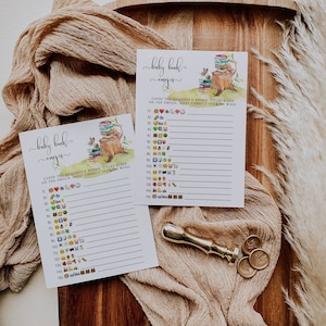 Puede incluir: Dos tarjetas de juego imprimibles para una fiesta de bienvenida al beb&eacute; con tem&aacute;tica de bosque. Las tarjetas muestran una ardilla sentada en un toc&oacute;n de &aacute;rbol con una pila de libros. El juego se llama "Baby Book Emojis" y pide a los jugadores que adivinen los t&iacute;tulos de los libros infantiles en funci&oacute;n de los emojis.