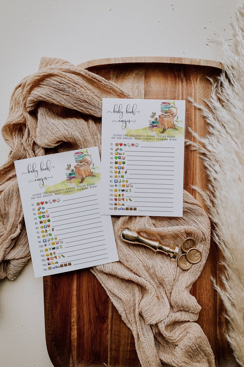 Puede incluir: Dos tarjetas de juego imprimibles para una fiesta de bienvenida al beb&eacute; con tem&aacute;tica de bosque. Las tarjetas muestran una ardilla sentada en un toc&oacute;n de &aacute;rbol con una pila de libros. El juego se llama "Baby Book Emojis" y pide a los jugadores que adivinen los t&iacute;tulos de los libros infantiles en funci&oacute;n de los emojis.
