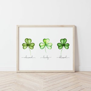 May include: A framed print with three watercolor shamrocks, each with a different word underneath: "charmed", "lucky", and "blessed".