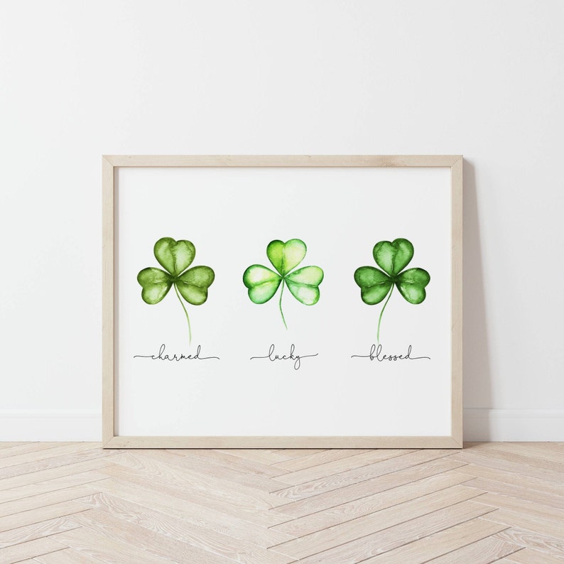 May include: A framed print with three watercolor shamrocks, each with a different word underneath: "charmed", "lucky", and "blessed".