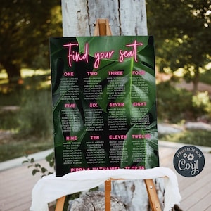 May include: A rectangular wedding seating chart sign featuring a dark green monstera leaf background with bright pink neon-style text. The sign displays the heading Find your seat, table numbers one through twelve with guest names, and the text Pippa & Nathaniel 12.02.26.
