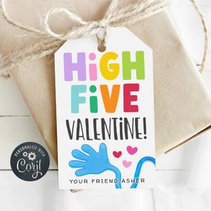May include: A gift tag with the words "HIGH FIVE VALENTINE!" in colourful letters. A blue hand graphic and three pink hearts are also on the tag. The tag is attached to a wrapped gift with twine.