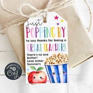 May include: A gift tag with the text "Just Popping By to say thanks for being a GREAT TEACHER!" in colorful letters. The tag features a watercolor illustration of popcorn and an apple. The tag is tied to a wrapped gift with twine.
