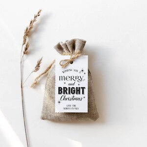 May include: A white gift tag with black text that reads "Wishing you a merry and bright Christmas" with stars and the words "Love the Rowan Family". The tag is tied to a small burlap bag.