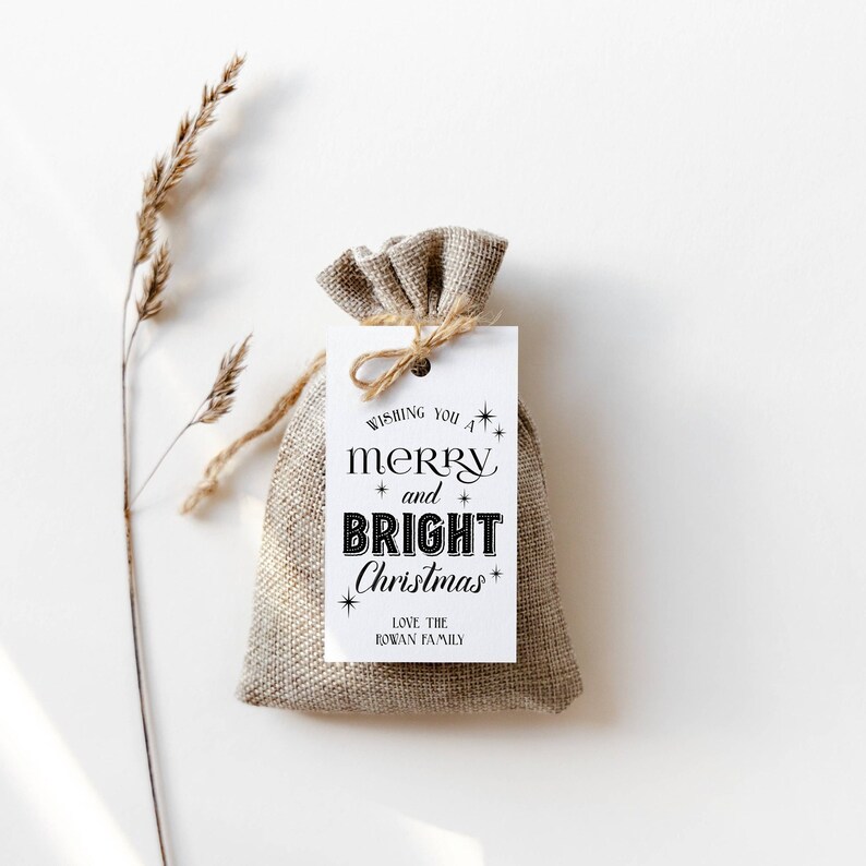 May include: A white gift tag with black text that reads "Wishing you a merry and bright Christmas" with stars and the words "Love the Rowan Family". The tag is tied to a small burlap bag.
