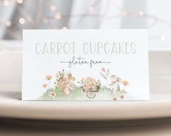 May include: A white card with the text "CARROT CUPCAKES - gluten free" in green text. The card features a watercolor illustration of two bunnies carrying baskets of flowers and a third bunny pulling a wheelbarrow full of flowers.