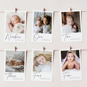 May include: A set of six white photo cards with black text and images of a baby at different ages. The cards are hung on a string with clothespins. The text on the cards reads "Newborn 10.10.23", "One Month", "Two Months", "Three Months", "Four Months", and "Five Months".
