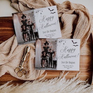 May include: Two rectangular Halloween greeting cards featuring a family photo with a ghost, spiderwebs, spiders, and bats. The text reads Happy Halloween! Love the Morgans, Nick, Sarah, Harvey, Rhian & Aiden 2022. A gold wax seal stamp and three seals.
